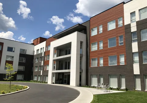 Residence facade with balconies, a curved driveway and outdoor chairs.