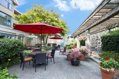 Garden patio with tables, chairs, red umbrellas and a pergola.