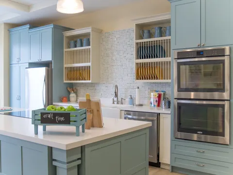 Kitchen with blue cabinets, an island, wall ovens and shelves of dishes