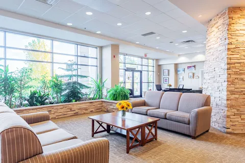 Sofas and a coffee table beside indoor plants and large windows