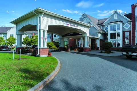 Covered driveway entrance beside blue siding, brick columns and lawns
