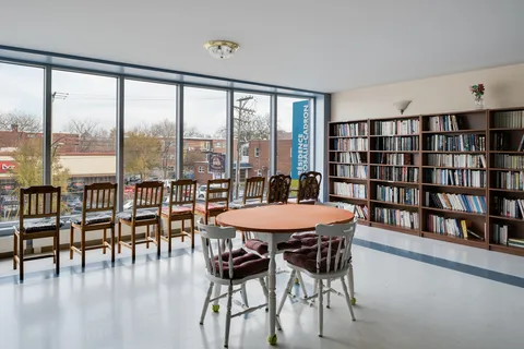 Library with bookshelves, chairs and a round table beside large windows
