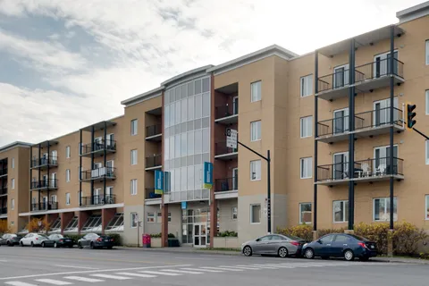 Multi-storey residence with balconies and parked cars beside a street