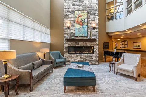 Room with a sofa, armchairs, an ottoman, a piano and a tall stone fireplace