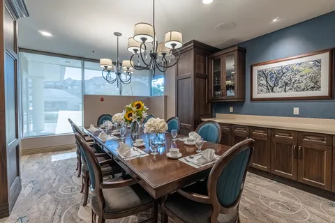 Dining room with a long set table, upholstered chairs, chandeliers and wooden cabinets