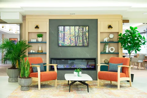 Sitting area with orange armchairs, a fireplace, landscape artwork and potted plants