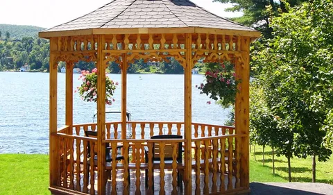 Wooden gazebo with chairs and hanging flower baskets beside a lake