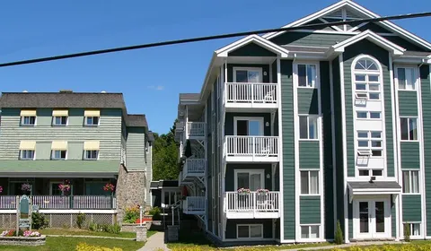 Green residence with white balconies, peaked roofs, an entrance and a lawn