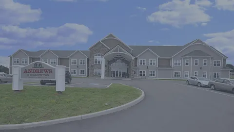 Multistorey building with a central covered entrance, lawn, trees and parked cars