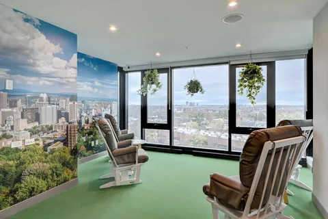 Rocking chairs beside large windows and a cityscape wall mural.