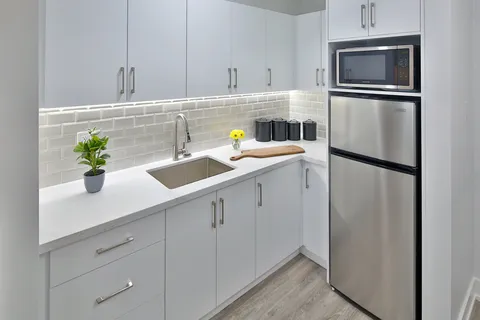 Kitchenette with white cabinets, sink, refrigerator and microwave.