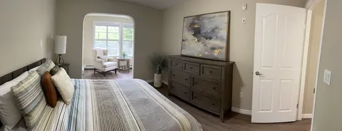 Bedroom with a striped bedspread, dresser and adjoining windowed sitting area