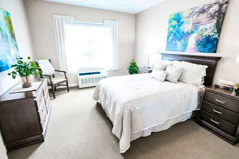 Bedroom with a white bed, dresser, bedside tables and a large window