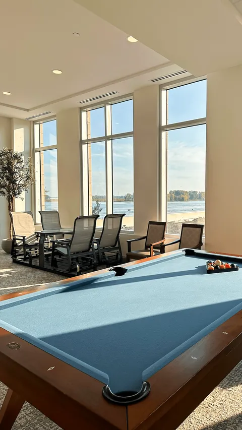 Billiard table beside tall windows and lounge chairs.