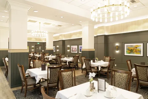 Dining tables with white tablecloths and upholstered chairs beneath chandeliers