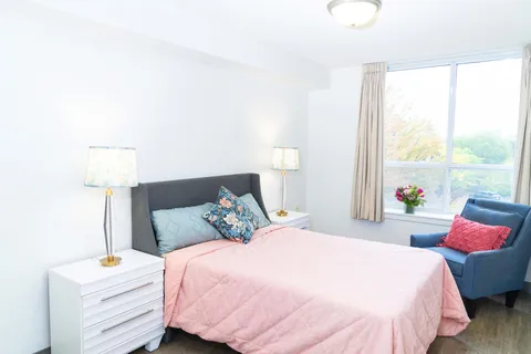 Bedroom with a pink bedspread, bedside drawers and a blue armchair