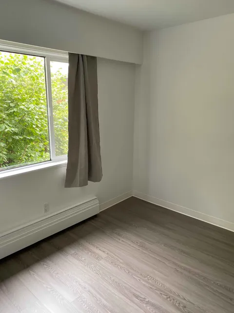 Empty room with a large window, curtains and pale wooden flooring