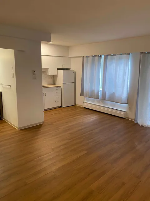 Empty room with a kitchenette, wooden floor and curtained windows