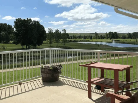 Covered deck with a red table overlooking lawn, trees and a pond