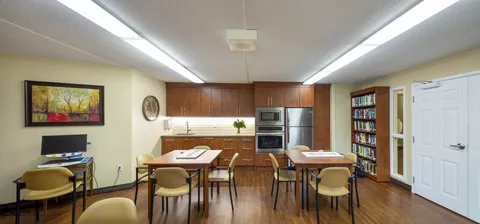Room with wooden tables, chairs, bookcases and a kitchen