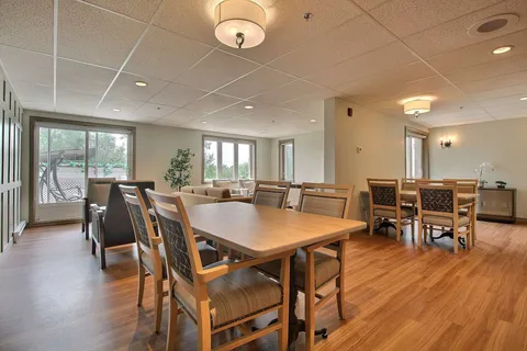 Common room with wooden tables and chairs beside windows.