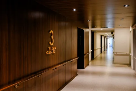 Corridor with wood-panelled walls, ceiling lights, handrails and room doors