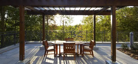Wooden patio table and chairs beneath a pergola beside trees