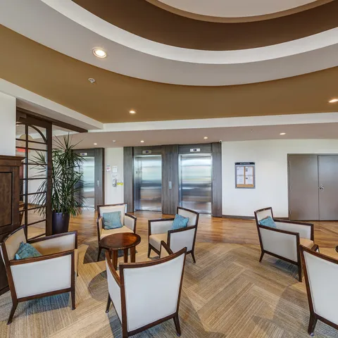 Armchairs and round side tables beneath a curved ceiling beside a lift