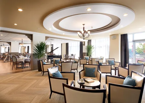 Open seating area with armchairs, round tables, a grand piano and large windows