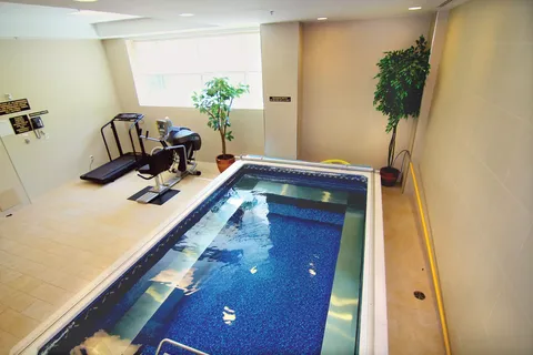 Small indoor pool beside exercise equipment and potted plants