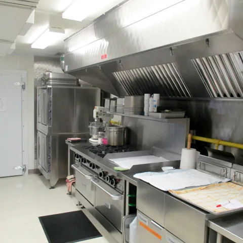 Commercial kitchen with a stove, steel counters and an extractor hood.