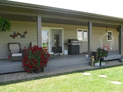 Covered terrace entrance with chairs, hanging flowers and a barbecue.