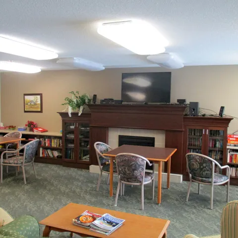 Common room with a fireplace, television, bookshelves and tables.
