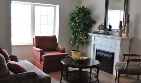 Armchairs and a round table beside a fireplace and a window