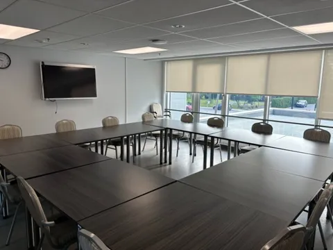 Room with tables arranged in a square, chairs and a blank wall-mounted television