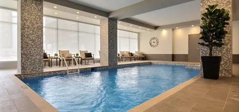 Indoor pool with loungers beside large windows.
