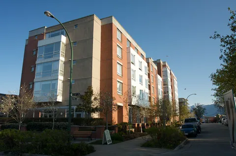 Multi-storey brick residence with large windows beside a tree-lined street.