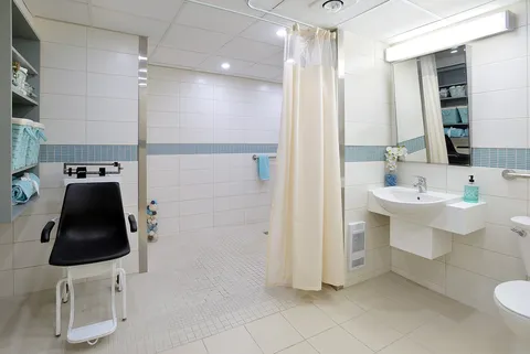 Accessible bathroom with a shower curtain, washbasin, toilet and a chair scale