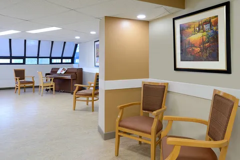 Seating area with wooden armchairs, a piano and framed landscape artwork