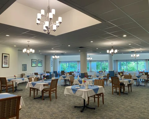 Dining room with wooden chairs, white and blue tablecloths, chandeliers and large windows