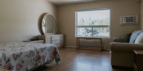 Bedroom with a floral bedspread, dresser, armchair and large window