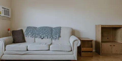 Sitting area with a cream sofa, wooden shelving and an air conditioner