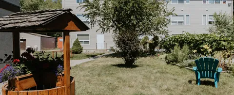 Garden with a wooden wishing well, lawn, flower beds and a green chair
