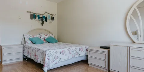 Bedroom with a floral bedspread, white dressers and an oval mirror