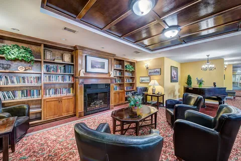 Library with bookcases, upholstered chairs and a fireplace.
