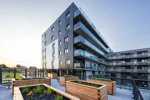 Raised wooden garden beds on a terrace beside a residence with balconies