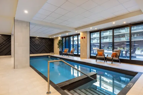 Indoor swimming pool with handrails and chairs beside windows