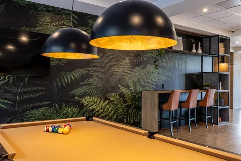 Pool table beneath black pendant lights beside bar stools