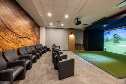 Room with leather chairs and a golf simulator showing a course