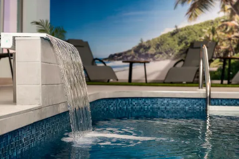 Indoor pool with a water cascade, handrail and tropical beach mural